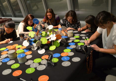 students gathered around table drawing on colorful participatory coasters