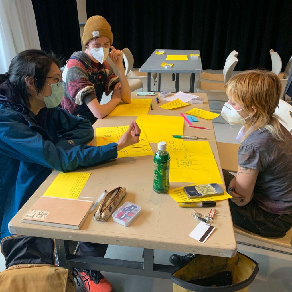 Design students sit around a table working sketching on yellow paper